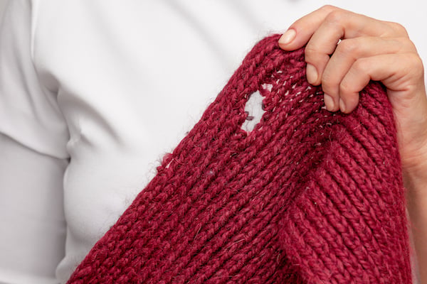 Woman's hand holding a scarf with holes made by moths