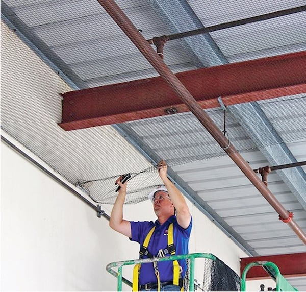 Man installing bird netting, standing on a scissor lift