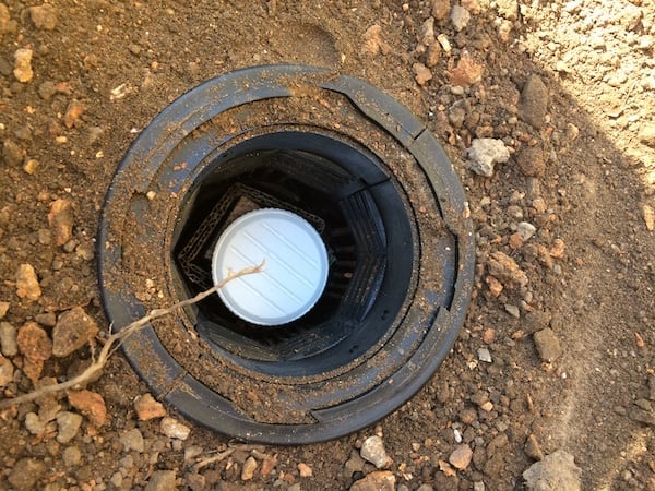 A compressed cellulose tablet placed on top some timber monitors, which are wrapped in cardboard. They are placed in a hole in the ground