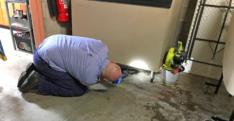 Man looking underneath a fridge with a torch