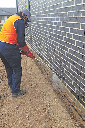Man spraying a black pipe which is part of a termite reticulation system