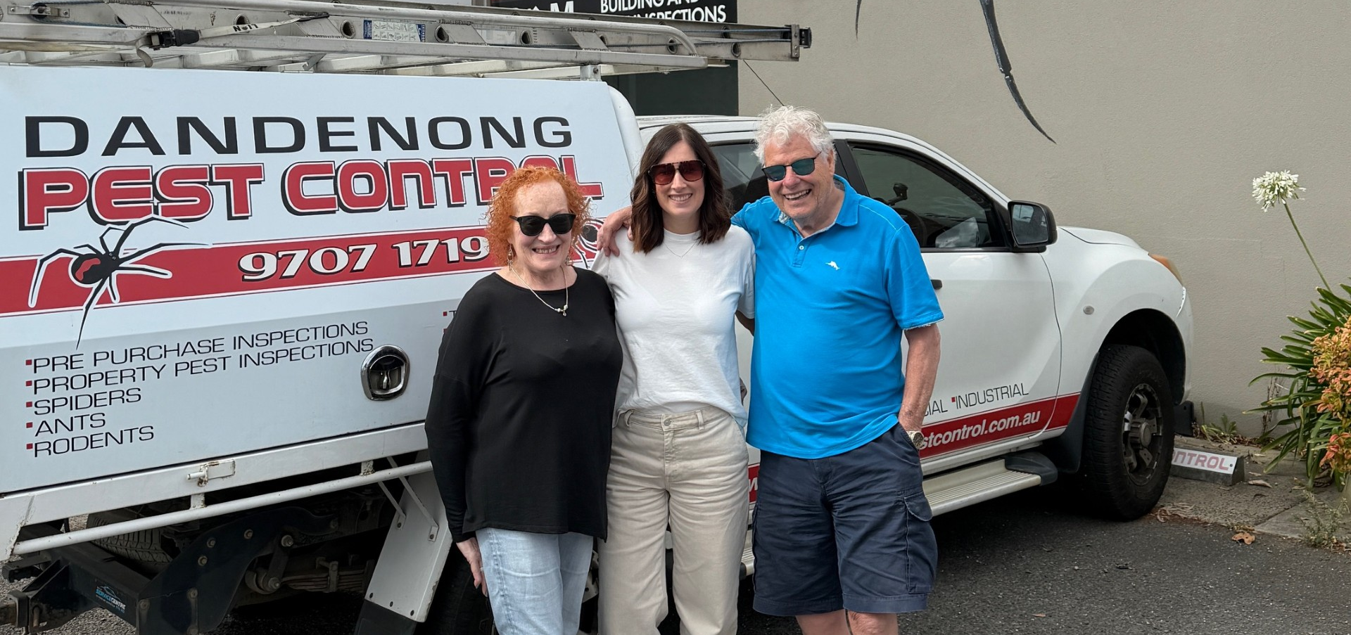 Lady in a white t-shirt and sunglasses with her parents either side of her, standing in front of a branded work vehicle