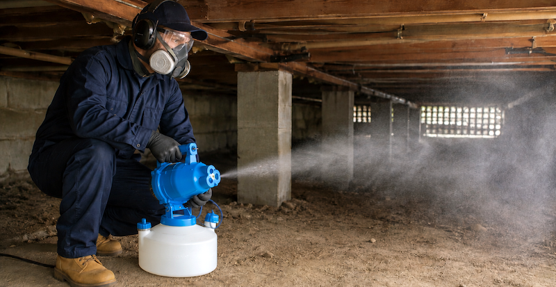 A man holding misting equipment underneath a house